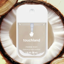Load image into Gallery viewer, A bottle of Touchland Hand Sanitizer Mist sits on a halved coconut, highlighting its delicately scented, clear liquid against the coconut’s white interior and brown shell for irresistibly hydrated hands.
