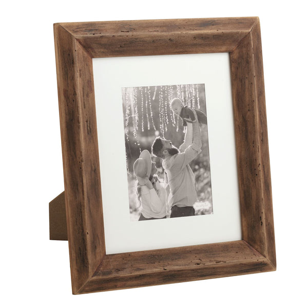 The Reclaimed Matte Wood Frame displays a black-and-white photo of two adults and a baby outdoors, with one adult lifting the baby under hanging lights. This eco-friendly frame is perfect for rustic home decor and stands easily on any flat surface.