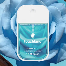 Load image into Gallery viewer, A bottle of Touchland Hand Sanitizer Mist, in clear blue with white text and a modern design, is displayed before a large blue rose—perfect for keeping hands fresh and delicately scented.