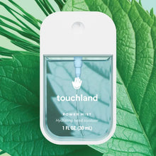 Load image into Gallery viewer, A clear rectangular Touchland Hand Sanitizer Mist bottle stands before overlapping green leaves, its logo and 1 fl oz (30 mL) label visible—ideal for hydrated hands with a delicately scented finish.