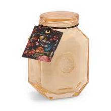 Load image into Gallery viewer, The 8oz Botanica Candle features cream-colored soy wax in a geometric light amber jar, embossed with a logo and finished with a black string tag labeled "Cotton &amp; Teak"—an elegant pick for luxurious candle enthusiasts.