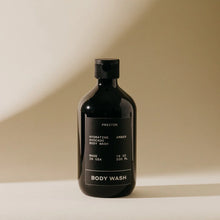 Load image into Gallery viewer, A dark bottle of Preston Body Wash stands on a light surface with a beige background. The label describes it as a moisturizing wash with hydrating avocado oil, made in the USA, and containing 16 oz (500 ml).