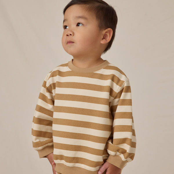 A young child with short dark hair looks upward while wearing the Oversized Crew Sweatshirt, made from organic cotton, standing against a plain light background.