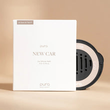 Load image into Gallery viewer, A white box labeled Pura Car Diffuser Refill sits next to a circular car air freshener refill with a sleek black and silver design, both displayed on a beige background.