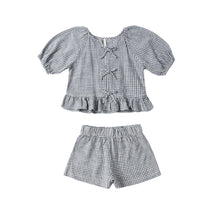 Load image into Gallery viewer, The Juniper Set is a children’s outfit with a blue and white marine gingham short-sleeve top featuring ruffled hem and bow details, paired with matching elastic-waist linen shorts, shown on a white background.