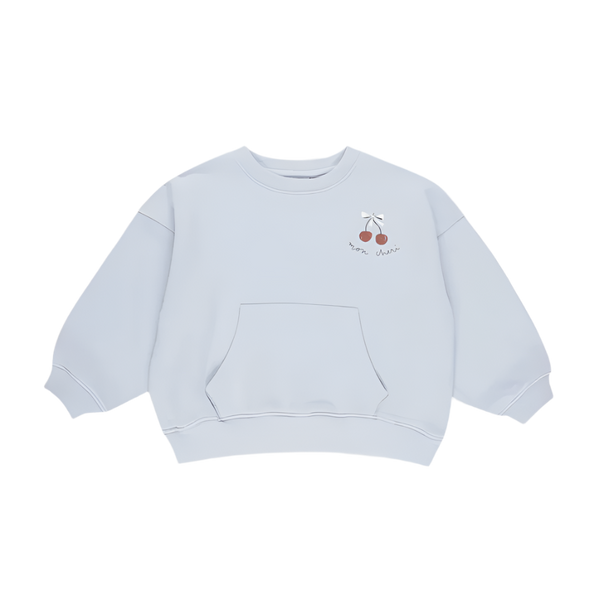 The Blue Sweatshirt (Cherry) features a light blue crewneck, loose fit, front kangaroo pocket, and a small cherry graphic with a white bow and text on the left chest. Perfect for transitional weather. Shown on a plain white background.