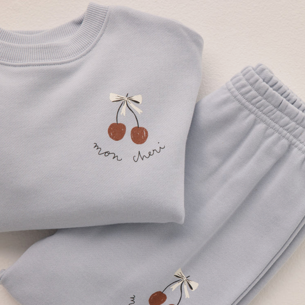 Folded light blue Blue Sweatpant (Cherry) set with baggy sweatpants and a sweatshirt, both featuring a small cherry graphic, cream bow, and cursive "mon cheri" text.