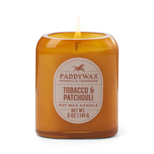 Load image into Gallery viewer, A lit 5oz Vista Candle in brown glass displays its luxurious tobacco &amp; patchouli fragrance on a white background.