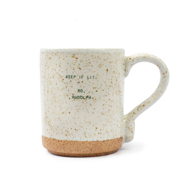 The Seasonal XO Mug is a white speckled ceramic mug with a natural clay bottom, curved handle, and green text: KEEP IT LIT. XO, RUDOLPH—bringing festive cheer and holiday quotes for oversized coffee mug fans.