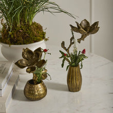 Load image into Gallery viewer, Two Golden Cast Aluminum Flower &amp; Pot pieces with metal floral designs and small flowers sit on a white marble table, creating a charming spring display beside a stack of books and a white planter with grass and moss.