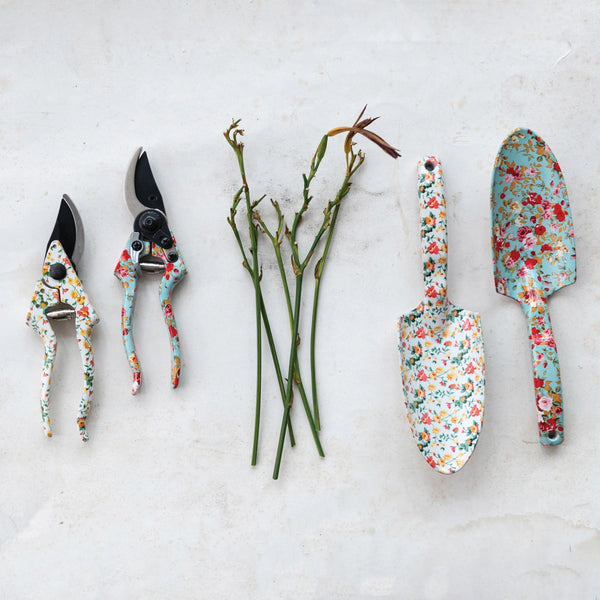 Creative Co-Ops Flowered Garden Tools: 2 Styles feature two floral-patterned pruning shears and aluminum tools, arranged with pruned rose stems on a light surface to add vibrant style to your gardening routine.