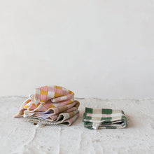Load image into Gallery viewer, A stack of folded pastel checked and plaid cotton Dish Cloths w/ 4 Checked &amp; Plaid Styles sits on the left, next to two green and white checkered cloths, all placed on a light textured surface with a plain white background.