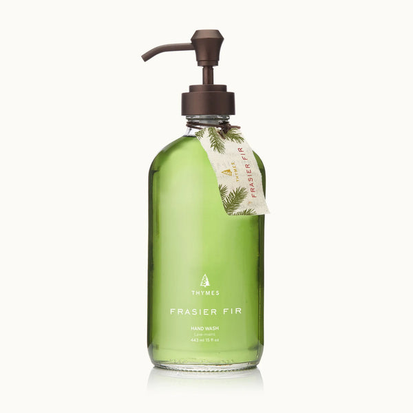 A clear glass pump bottle from the Frasier Fir Home Care Collection holds green hand wash and features a pine-decorated tan tag—a signature winter fragrance for your home.