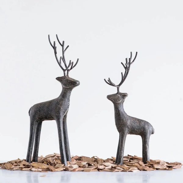 The Cast Iron Deer sculptures, featuring tall stylized antlers, stand on wood chips against a white background—an eye-catching accent for rustic home décor.