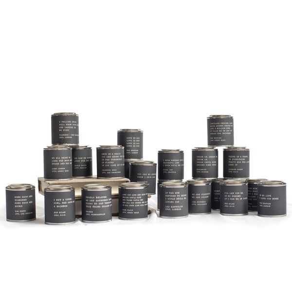 Lit Decor and Gift’s Legends Candles—Pick From 20 Quotes—are displayed in black jars with white text labels, arranged in tiers. Each vegan candle features a unique phrase. The background is plain white.