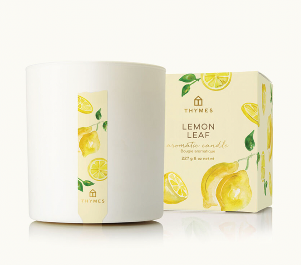 A white Thymes Aromatic 8 oz Candle by Lit Decor and Gift sits beside a watercolor lemon-decorated box, offering an uplifting, refreshing home fragrance with a clean burn.