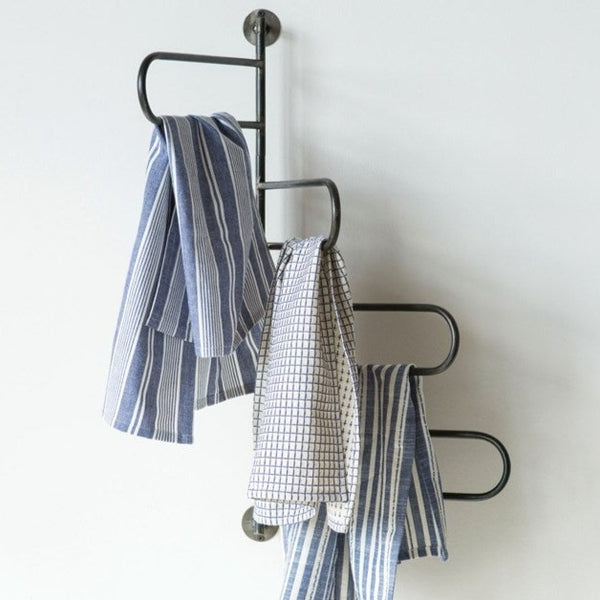 Three kitchen towels—two blue with white stripes and one white with a black grid—hang on a Lit Decor and Gift Swivel Wall Rack mounted to a light wall.